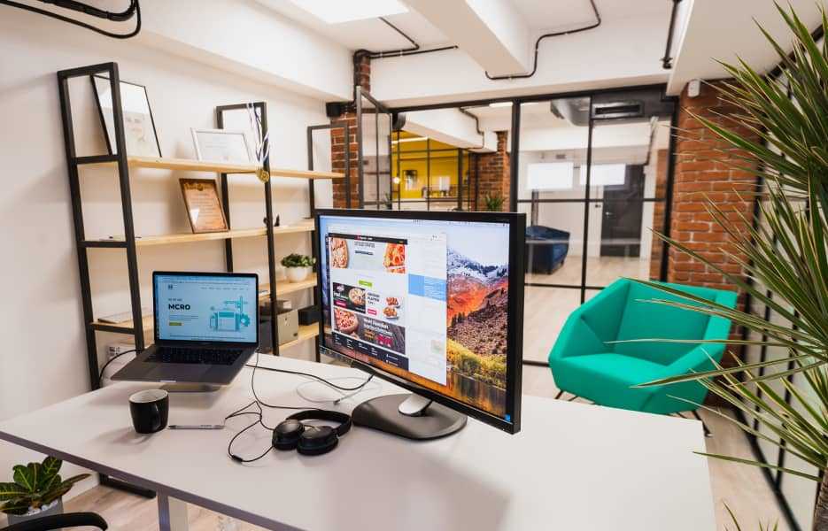 Turned on monitor and silver laptop on a white desk inside an office